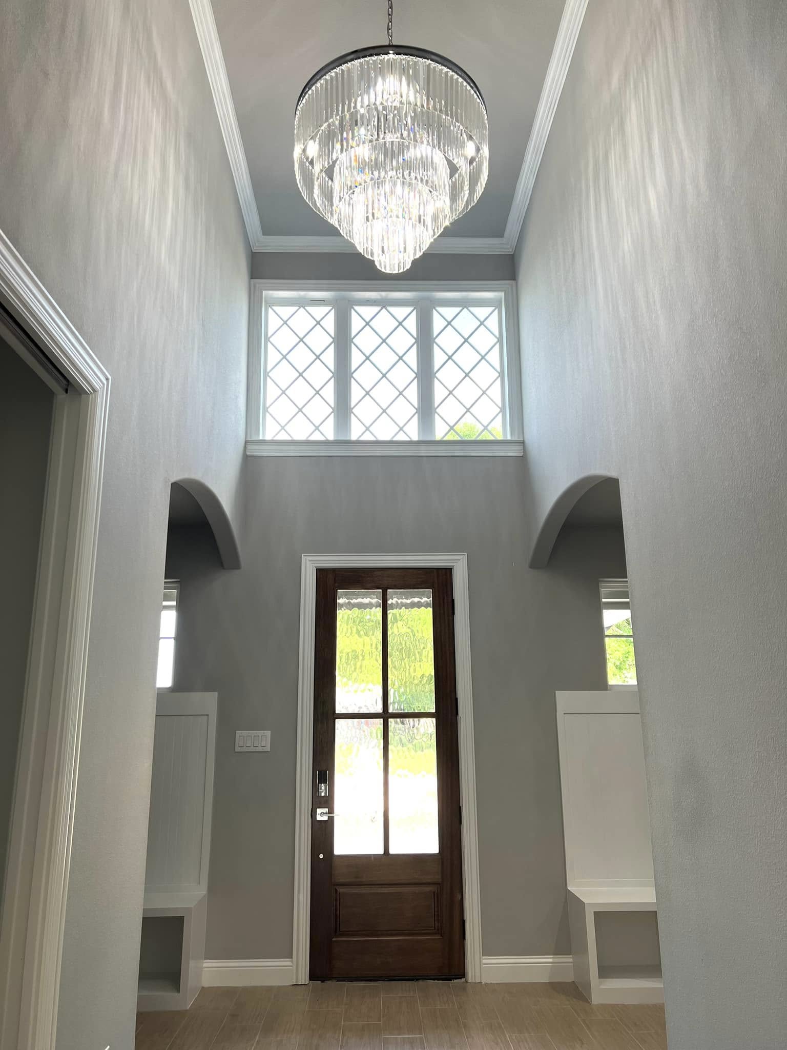 Grand entryway of a luxury custom home in Navarro County, TX featuring a crystal chandelier, arched doorways, and custom woodwork.