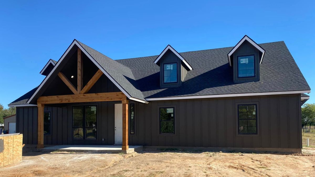 Custom home built by premier custom home builders in Athens TX featuring dark vertical siding, timber gable porch, and steep roof pitch.