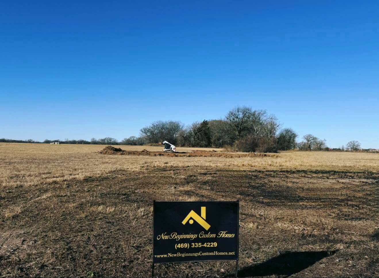 A job site yard sign for New Beginnings Custom Homes on a cleared land parcel in Athens, Texas.