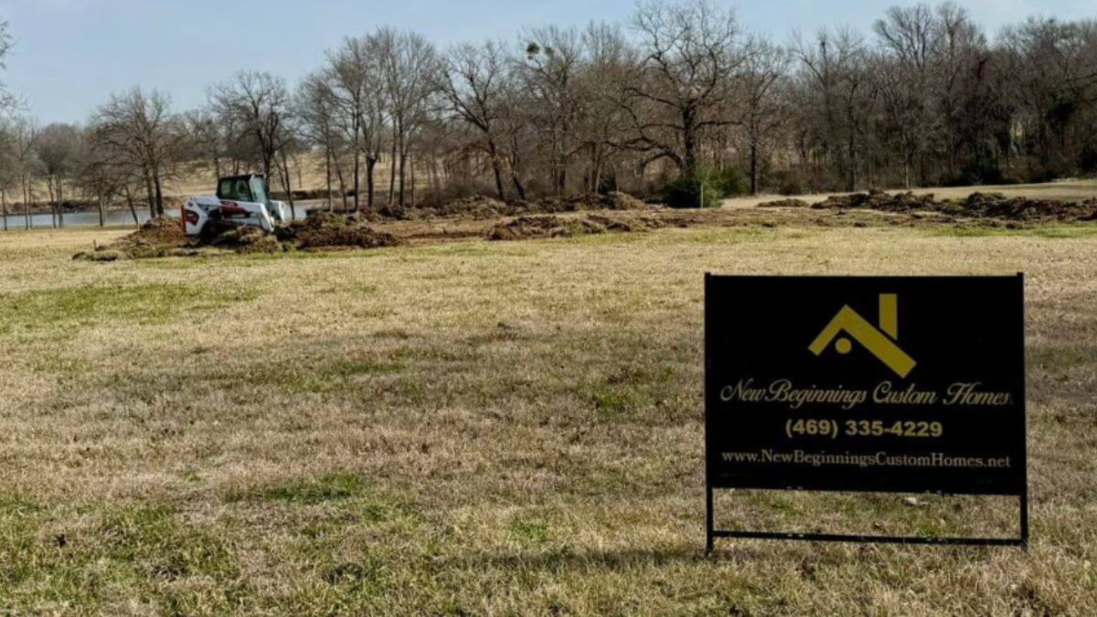 A New Beginnings Custom Homes sign stands on a cleared build site in Canton, Texas with a skid steer excavating in the background.